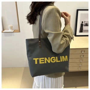 Detail of grey canvas tote bag with yellow logo, leather handles and rivet accents