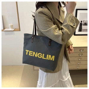 Detail of grey canvas tote bag with yellow lettering and brown leather handles