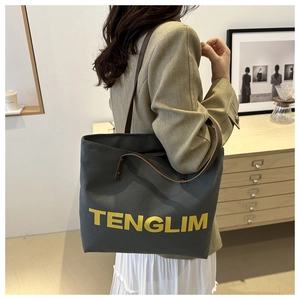 Detail of grey canvas tote bag with yellow lettering and brown leather straps