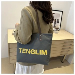 Detail of grey canvas tote bag with leather handles and yellow TENGLIM text print