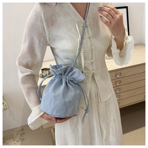 Detail of light blue drawstring bucket bag featuring natural textured fabric and strap