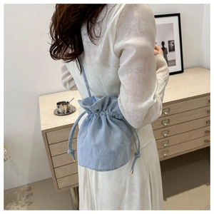 Light blue drawstring bucket bag with pleated texture and thin shoulder strap worn by model
