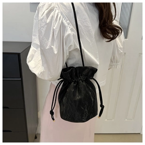 Detailed view of black drawstring bucket bag featuring pleated texture and gold hardware