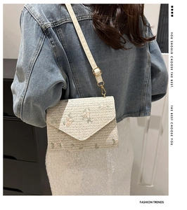 Detail of beige straw crossbody bag with floral embroidery worn by a model in denim