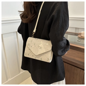 Mannequin portant un sac enveloppe tissé crème avec broderie de feuilles vertes et bandoulière