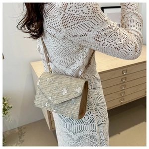 Detail of woven beige shoulder bag featuring pastel floral embroidery and sleek strap
