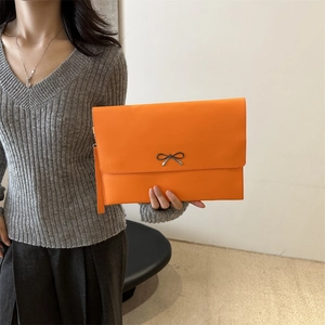 Chic orange envelope bag with black bow buckle and wrist strap shown by model