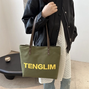 Large olive green canvas tote bag with yellow letters and brown shoulder straps