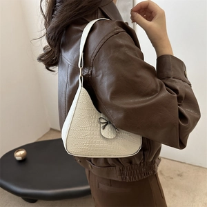 Sac hobo blanc à motif crocodile avec nœud noir porté à l'épaule par le mannequin