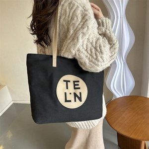 Minimalist black canvas tote bag with leather handles and round logo patch for women