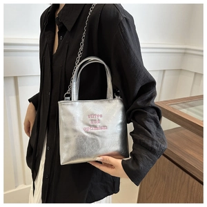 Dettaglio borsa tote argento metallizzato con ricamo rosa e tracolla a catena in metallo