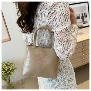 Dettaglio del ricamo 'strive and optimism' su una borsa tote beige con tracolla a catena