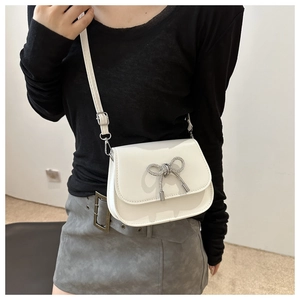 Detail of white matte leather crossbody bag with silver bow accent and adjustable strap