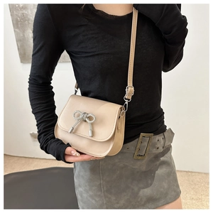 Close-up of beige crossbody saddle bag with a silver metallic bow decoration and long strap