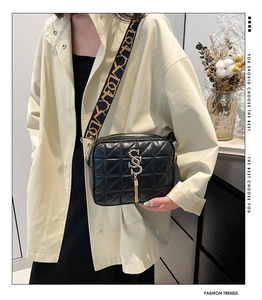 Detail of black quilted shoulder bag with patterned wide strap and gold tassel