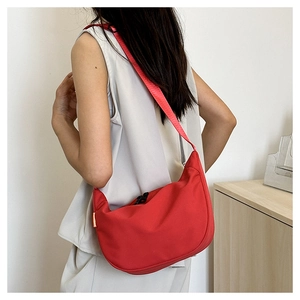 Red nylon crescent crossbody bag with adjustable strap worn by a model in a minimalist room