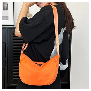 Detail of bright orange crescent crossbody bag in nylon shown on model with black strap