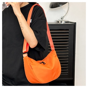 Detail of a bright orange nylon dumpling bag with adjustable wide strap worn by a model