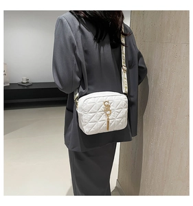 Close-up of a white quilted crossbody bag with gold S-logo, tassel and wide fabric strap