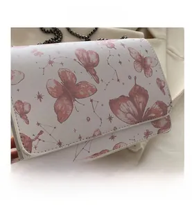Gros plan du sac bandoulière en cuir blanc avec motifs papillons et chaîne métallique