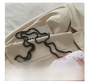 Détail du sac bandoulière blanc à imprimé papillon avec chaîne métallique sur costume beige