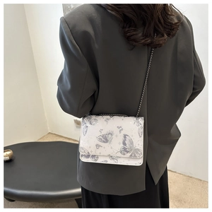 Detail shot of a stylish crossbody flap bag with butterfly prints and metal chain strap