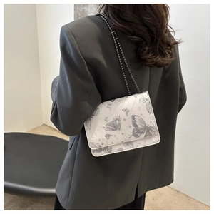 Detailed view of white crossbody bag with purple butterfly prints and metal chain strap
