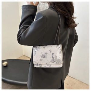 Detail of white chain crossbody bag with butterfly print worn over a black blazer
