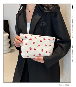 Close-up of strawberry print corduroy pouch held by model in black blazer