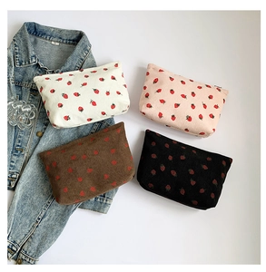 Flat lay of four strawberry print corduroy pouches in cream, pink, brown and black colors
