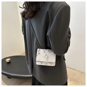 Detail of butterfly print square crossbody bag with chain strap worn on black blazer