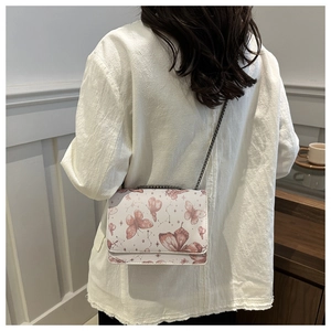 Close-up of white crossbody bag with pink butterfly prints and metal chain strap