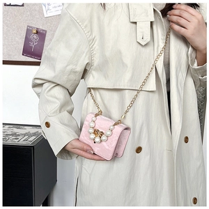 Detail of pink faux leather crossbody bag with pearls and gold heart clasp on model