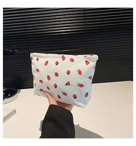 Close-up of white corduroy pouch with red strawberry print and smooth metal zipper