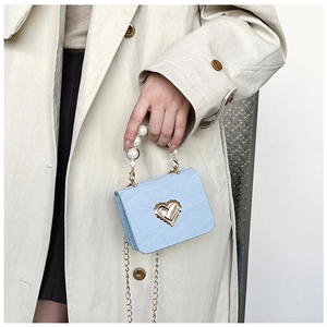 Detail of light blue mini bag with pearl handle and golden heart lock on trench coat