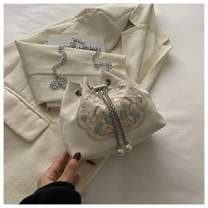 Detail view of floral embroidery and pearl pendants on cream bucket bag