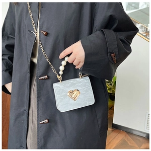Close-up of pearl handle and golden heart clasp on mini shoulder bag with pleated texture
