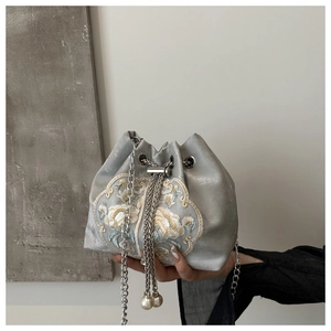 Detail of floral embroidery on silver satin bucket bag with pearl drawstring and metal chain