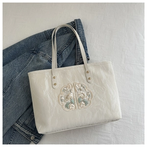 Close-up of a white tote bag featuring delicate floral embroidery and glossy texture