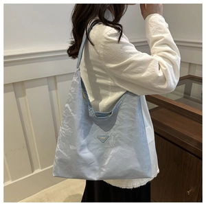 Dettaglio della trama in tessuto plissettato azzurro e placca logo in metallo della borsa tote