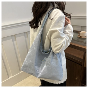Dettaglio borsa tote azzurra plissettata con logo a triangolo indossata da modella