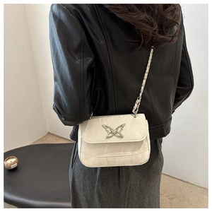 Detail of creamy white crossbody bag with silver butterfly buckle on a black jacket