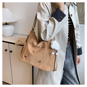 Détail du sac bandoulière beige plissé avec papillons et breloque nuage pelucheux sur un mannequin