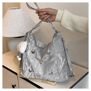 Détail du sac bandoulière argenté plissé avec papillons métalliques et charme blanc
