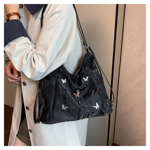 Détail d'un sac bandoulière noir avec texture plissée et ornement papillon argenté