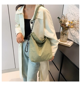 Close-up of a sage green minimalist crossbody tote bag worn by a model in a trench coat