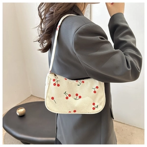 Detail of corduroy shoulder bag with cherry print and golden zipper on white fabric