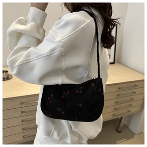 Detail of black corduroy shoulder bag featuring red cherry prints worn by a model