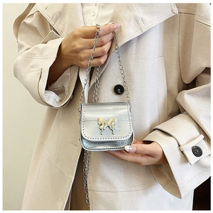Close-up of silver mini chain bag with metallic butterfly accent on beige trench coat