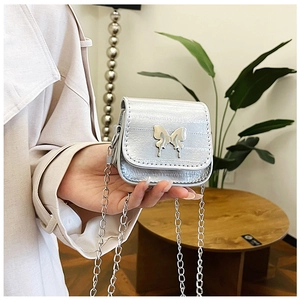 Close-up of a mini silver chain bag with a metallic butterfly charm being held by hand